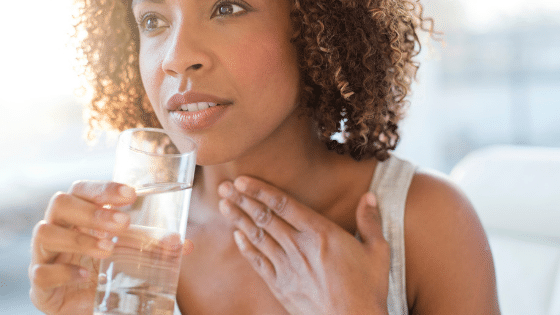 A woman with her hand placed on her throat while holding a glass with water.