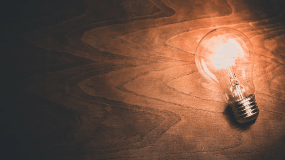 A turned on lightbulb lying on a wood floor.