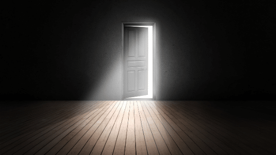 A black wall with a black door opening and a bright light coming through it.