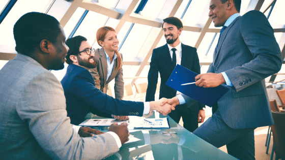 Two men shaking hands while being surrounded by other people.