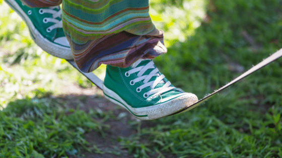 A human walks on a slack line with green converse.