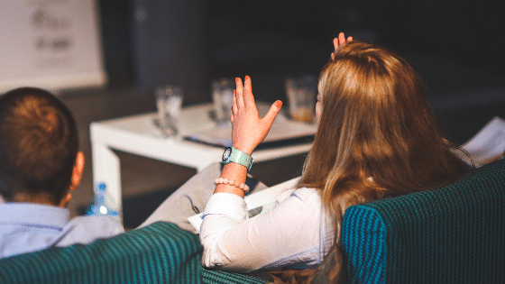 A woman sitting down while having her hands up looking at a screen.