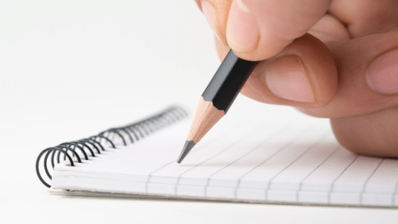 A hand holding a pen on a black note pad.