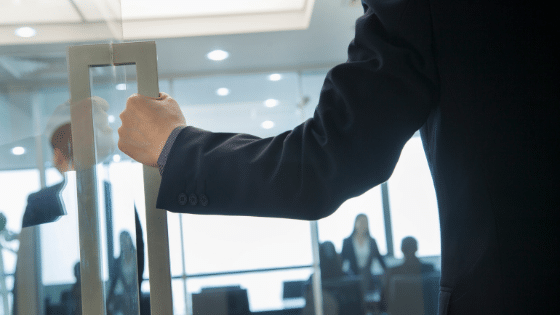 A person holding the a big square knob of a glass door.