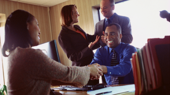 A group of smiling business people with two shaking hands enthusiastically