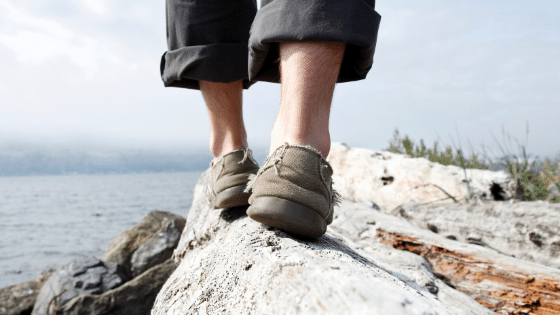 A person's legs walking on the edge of a rock and the ocean on the background.