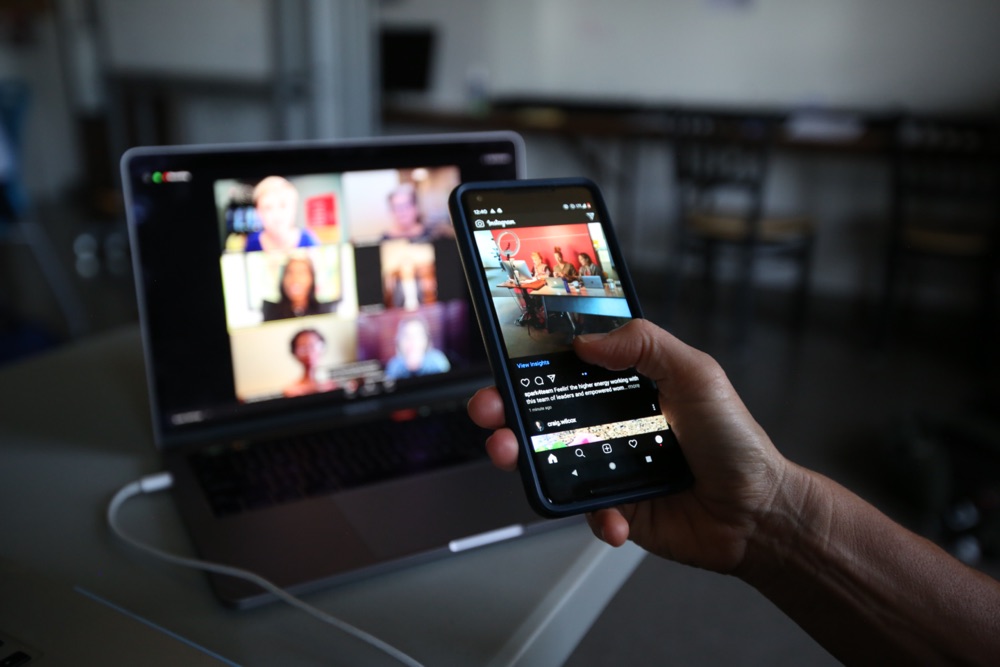 A hand holding a phone and a laptop on the background.